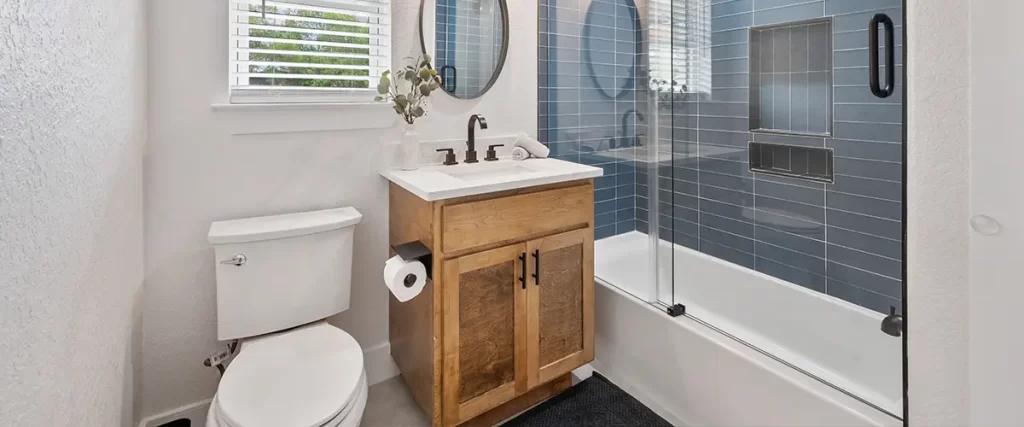 Updated bathroom renovation featuring blue tile shower, glass doors, and custom wood vanity