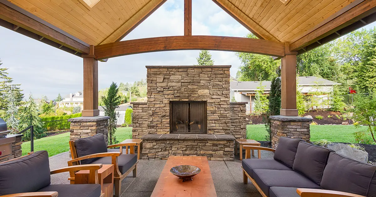Covered outdoor living space with stone fireplace, timber ceiling, and custom patio cover installation.