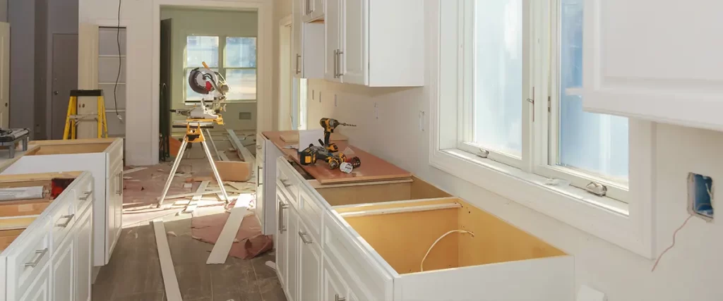 Kitchen renovation in progress with custom cabinets, trim installation, and contractor tools on site.