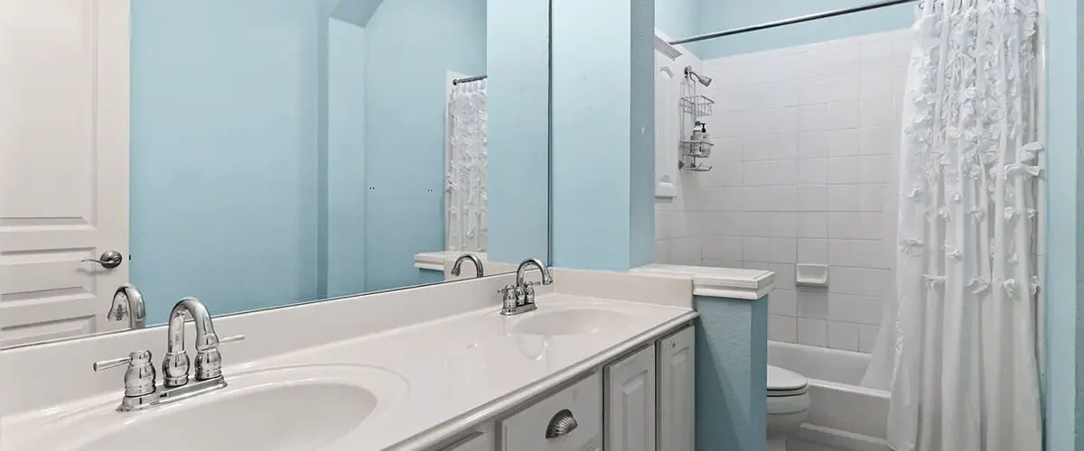 Bathroom before conversion with blue walls, white vanity, and tub shower combination