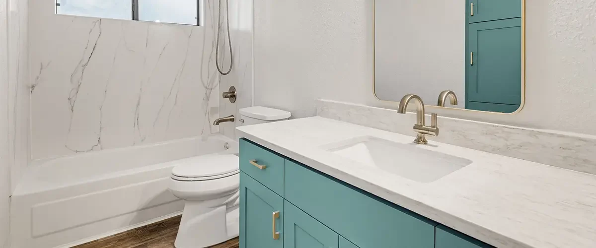Modern bathroom conversion with teal vanity, quartz countertop, and updated tub surround