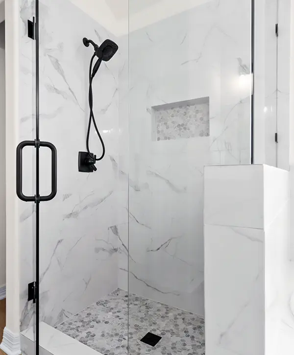 Modern walk-in shower with marble-look tile, glass enclosure, black fixtures and pebble tile floor