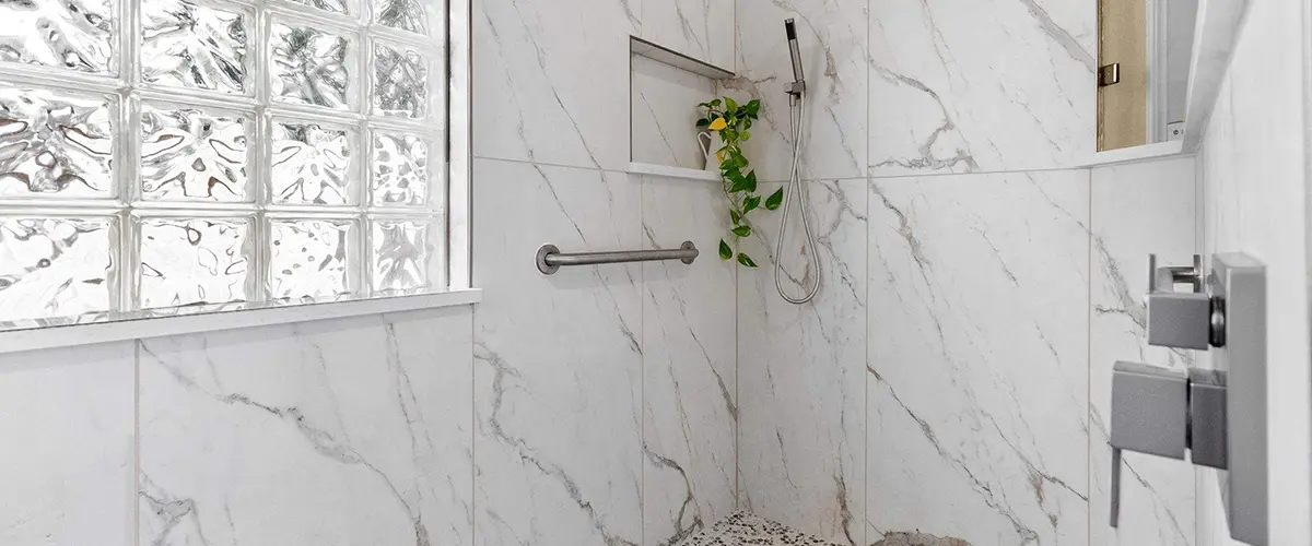 Walk-in shower remodel with marble-look tile, rainfall showerhead, glass block window and pebble floor
